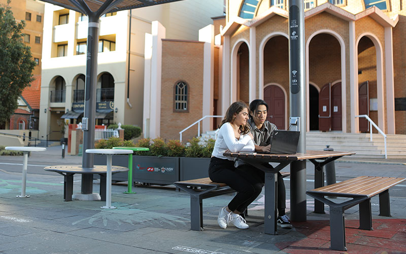 Young man and woman sitting at table working outside