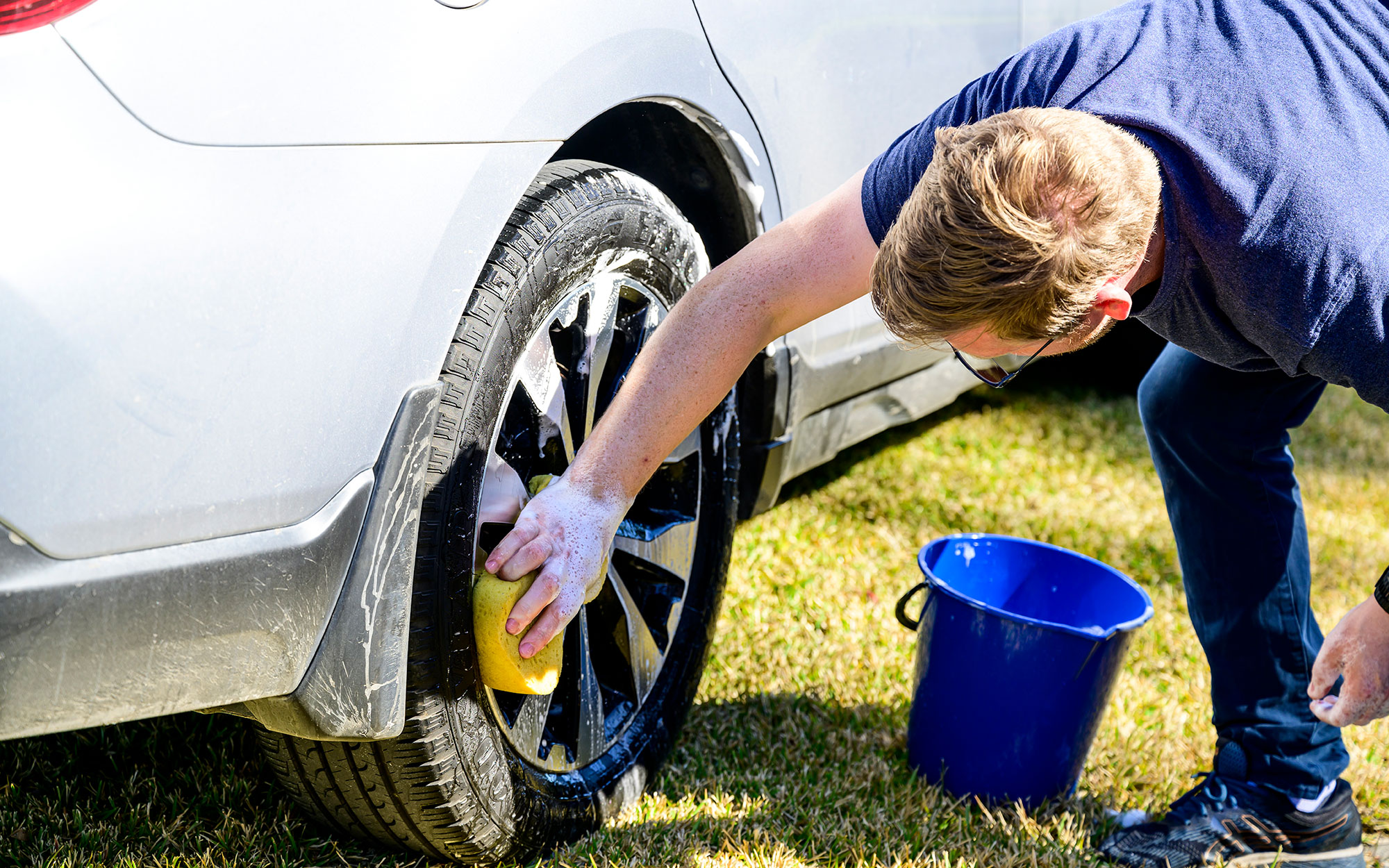Man washing car tyre with bucket and sponge